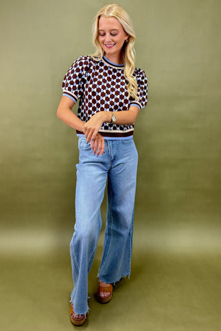 Woman wearing a patterned top and blue jeans against a green background