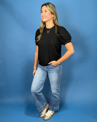 A woman modeling a red ribbed short-sleeve top with puff sleeves, paired with blue jeans