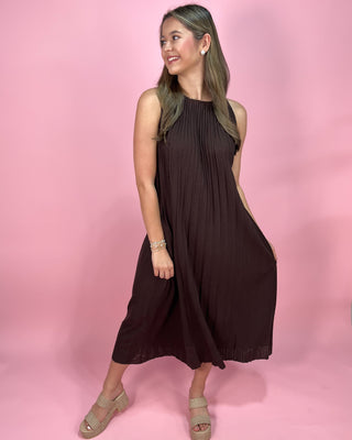 Woman wearing a brown sleeveless dress against a pink background