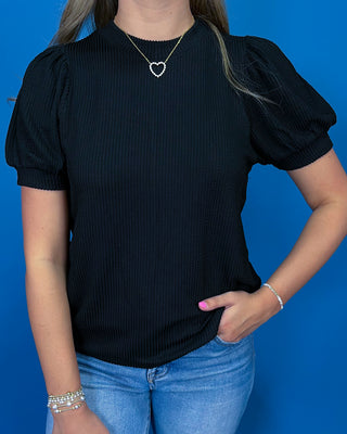A woman modeling a red ribbed short-sleeve top with puff sleeves, paired with blue jeans