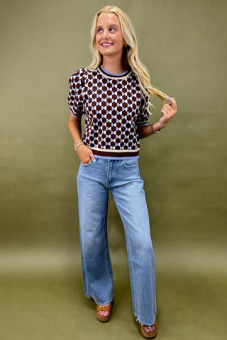 Woman wearing a patterned top and blue jeans against a green background