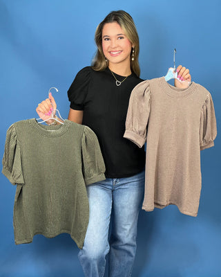 A woman modeling a red ribbed short-sleeve top with puff sleeves, paired with blue jeans