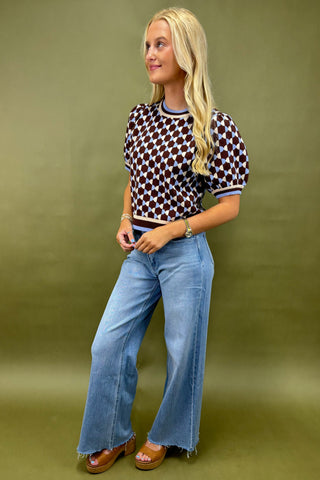 Woman wearing a patterned top and blue jeans against a green background