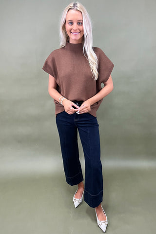 Woman wearing a brown top and dark blue jeans against a plain background