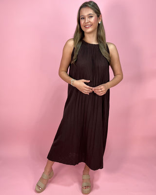 Woman wearing a brown sleeveless dress against a pink background