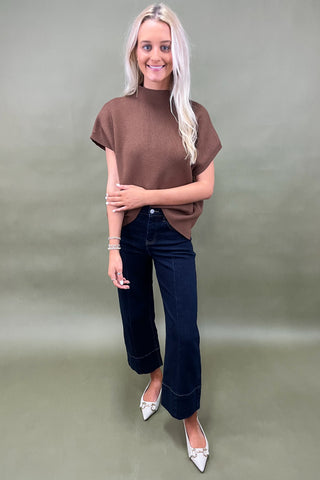 Woman wearing a brown top and dark jeans on a plain background