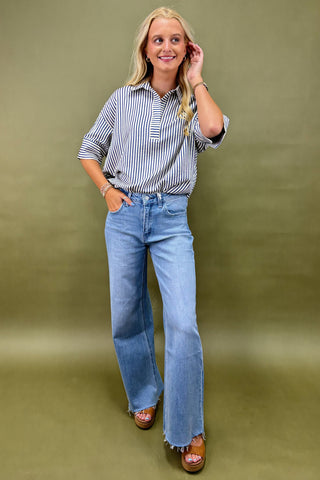 Woman wearing a striped shirt and blue jeans against a green background