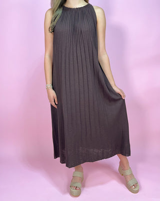 Woman wearing a dark brown pleated dress on a pink background