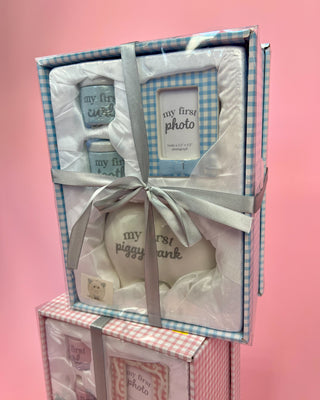 Baby gift set with photo frame, teether, and rattle in a checkered box on a pink background