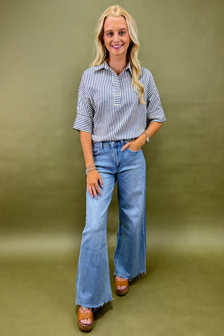 Woman wearing a striped shirt and blue jeans against a green background