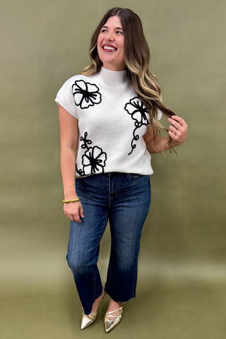 Woman wearing a white t-shirt with black floral designs and blue jeans against a green background