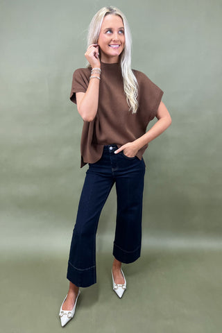 Woman wearing a brown top and dark jeans on a plain background