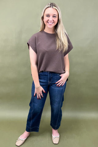 Woman wearing a brown top and blue jeans against a green background