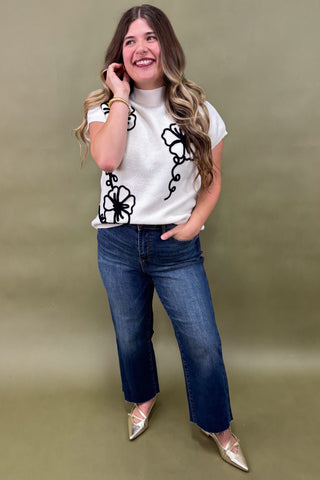 Woman wearing a white t-shirt with black floral designs and blue jeans on a green background