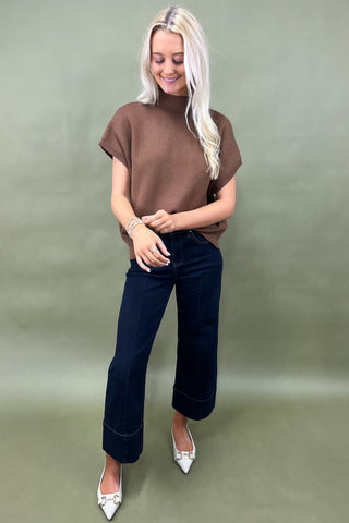 Woman wearing a brown top and dark jeans on a plain background