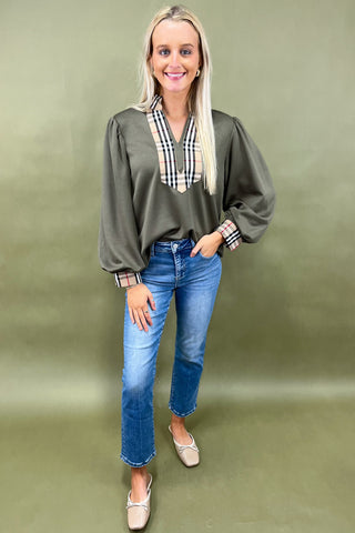 Woman wearing a green top with plaid accents and blue jeans on a green background