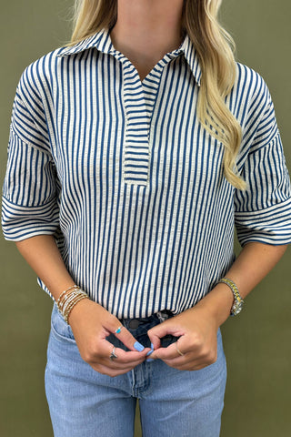 Person wearing a blue and white striped shirt with rolled-up sleeves and light blue jeans against a green background.