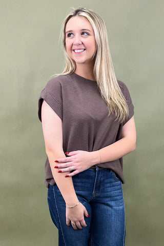 Woman wearing a brown top and blue jeans against a green background