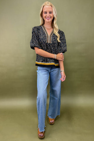 Woman wearing a black patterned top and blue jeans against a green background