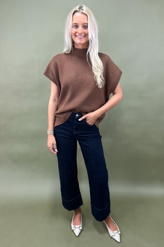 Woman wearing a brown top and dark jeans on a plain background