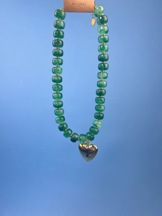 Green marbled resin bead necklace with polished gold heart pendant, gold-tone spacer accents, adjustable cord closure, and lightweight statement design available in multiple colors.