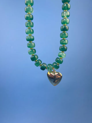 Green marbled resin bead necklace with polished gold heart pendant, gold-tone spacer accents, adjustable cord closure, and lightweight statement design available in multiple colors.