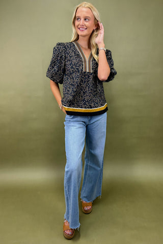 Woman wearing a patterned top and blue jeans against a green background