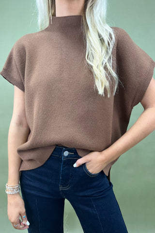 Person wearing a brown sweater and blue jeans against a light green background