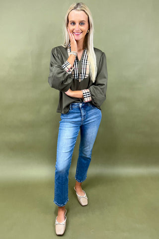 Woman wearing a green jacket and blue jeans against a green background
