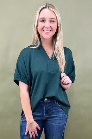 Woman wearing a green blouse and blue jeans against a beige background