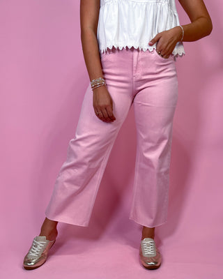 Person wearing pink jeans and a white top against a pink background