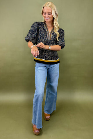 Woman wearing a patterned top and blue jeans against a green background