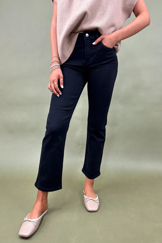 Person wearing navy blue pants and a beige top on a green background