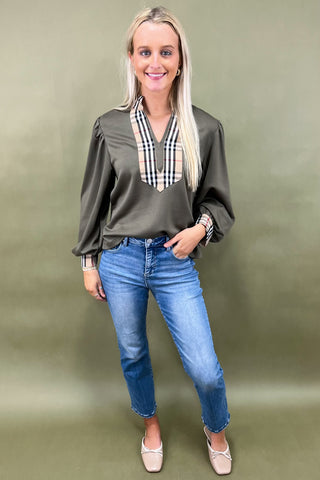 Woman wearing a green blouse with a plaid collar and blue jeans on a green background