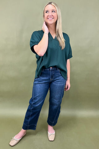 Woman wearing a green top and blue jeans against a green background
