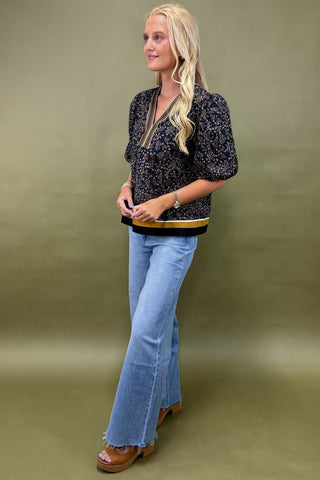Woman wearing a black floral top and blue jeans against a green background