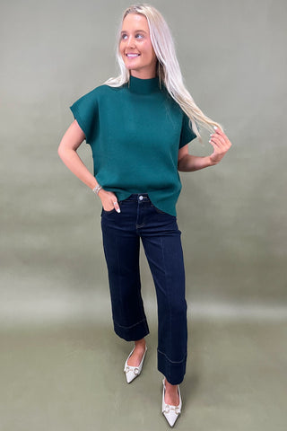 Woman wearing a green top and dark jeans on a plain background