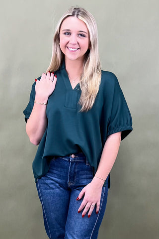Woman wearing a green blouse and blue jeans against a plain background