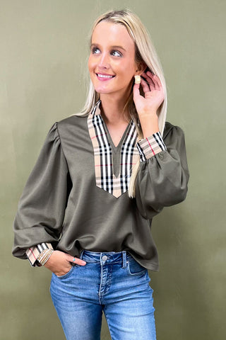 Woman wearing a green blouse with plaid accents and blue jeans against a green background
