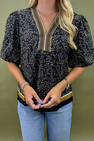 Woman wearing a dark floral blouse with a V-neck and short sleeves against a green background