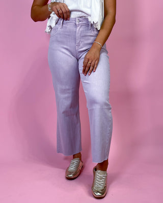 Person wearing light purple jeans and gold shoes on a pink background