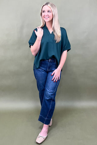 Woman wearing a green top and blue jeans against a plain background