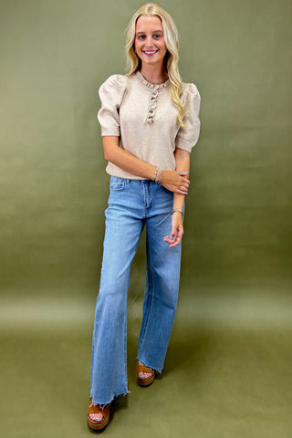 Woman wearing a beige blouse and blue jeans against a green background