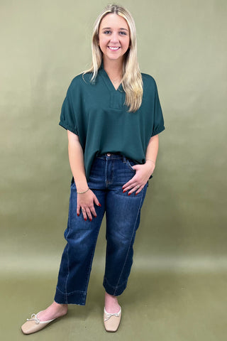 Woman wearing a teal shirt and blue jeans against a green background