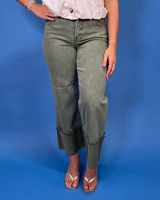 A model wearing olive green cropped jeans with frayed ruffle trim at the hem, paired with a white top