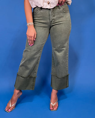 A model wearing olive green cropped jeans with frayed ruffle trim at the hem, paired with a white top