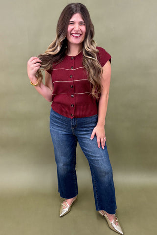 Woman wearing a red cardigan and blue jeans against a green background