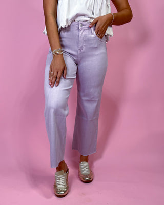 Person wearing light purple jeans and white sneakers on a pink background