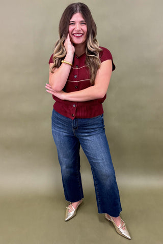 Woman wearing a red cardigan and blue jeans against a green background