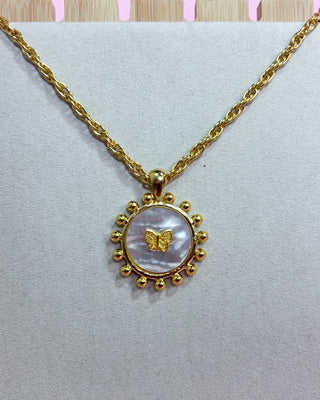 Gold necklace with a round pendant featuring a butterfly design on a light gray background